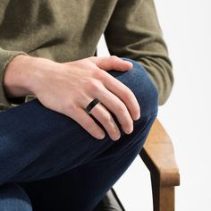 a person sitting in a chair with their hand on his lap and wearing a black ring