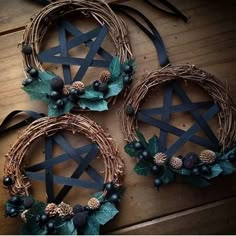 three wreaths with pine cones, berries and leaves are arranged on a wooden surface