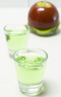 two shot glasses filled with green liquid and an apple on the table next to it