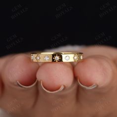 a woman's hand holding a gold wedding band with five diamonds on the side