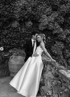 a bride and groom leaning against a stone wall in front of a large planter