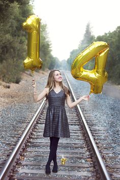 a woman holding two gold balloons standing on train tracks with the number four spelled out