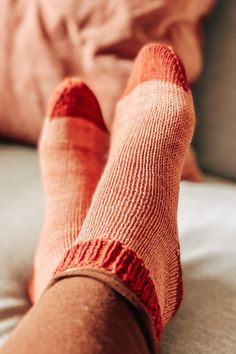 someone's feet with red socks on sitting on a couch next to a pillow