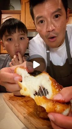 a man and boy eating food together in the kitchen with an adult pointing at them