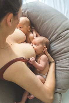 a woman holding two babys in her arms while laying on top of each other