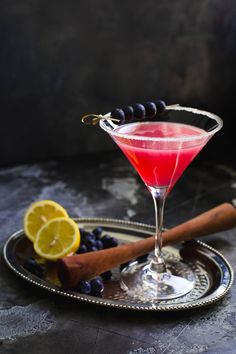 a red drink in a martini glass with blueberries and lemons on the side