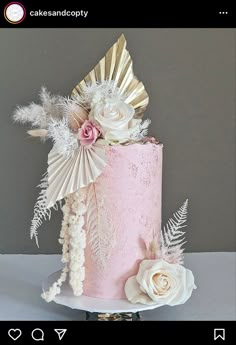 a pink cake with white flowers and feathers on it's side, sitting on a table