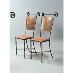 two chairs sitting side by side in front of a gray wall with an iron frame and wood seat