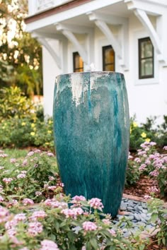 a large blue vase sitting in the middle of a flower garden next to a white house