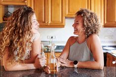 two women sitting at a kitchen counter with wine glasses in front of them smiling and looking into each other's eyes