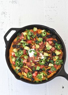 a pizza in a skillet topped with toppings and avocado on top