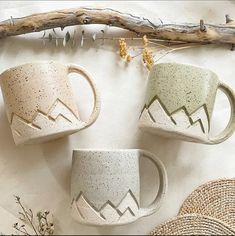 three coffee mugs with mountains on them sitting next to some twigs and dried flowers