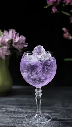 a glass filled with purple liquid next to flowers