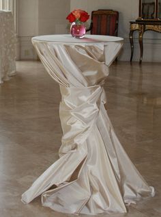 a white table with a vase on top of it and a chair in the background