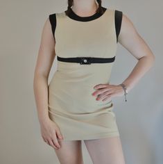 a woman with her hands on her hips wearing a beige dress and black leather belt