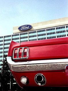 an old red ford truck parked in front of a tall building with a ford logo on it