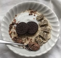 a bowl filled with cereal and cookies on top of a white table cloth next to a spoon