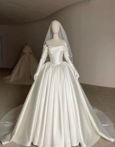 a white wedding dress on display in a room with mannequins behind it