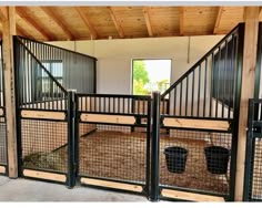 the inside of a horse stable with metal gates and hay in buckets on the floor