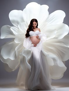 a pregnant woman in a white gown standing with her arms around the belly of a large flower