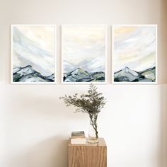 three paintings hang on the wall above a table with a vase and plant in it