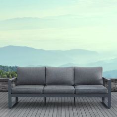 a gray couch sitting on top of a wooden floor next to a wall with mountains in the background