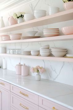 the shelves are filled with white dishes and pink vases on top of marble countertops