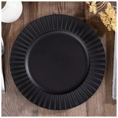 an empty black plate on top of a wooden table next to silverware and flowers