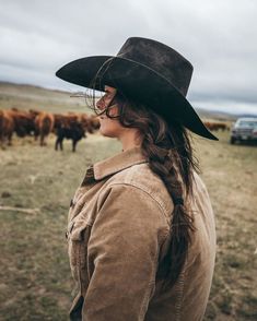 a woman wearing a cowboy hat standing in front of cows