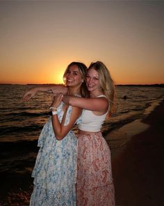 two women standing next to each other on a beach near the ocean at sunset with their arms around each other