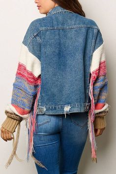 a woman wearing a jean jacket with fringes on the sleeves and back, standing in front of a white wall