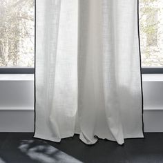 a white curtain with black trim hanging in front of a window, next to a tree