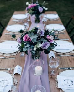 the table is set with white plates and purple flowers