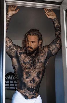 a man with tattoos on his body standing in front of a mirror and holding his hands up