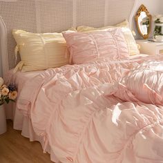 a bed with pink comforter and pillows on top of it next to a mirror