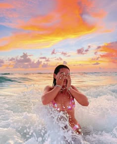 a woman in a bathing suit standing in the ocean with her hands on her face