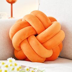 an orange knot pillow sitting on top of a white couch