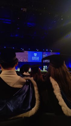 two people in graduation gowns looking at a screen