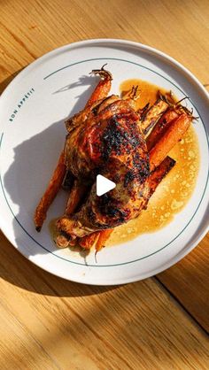 a white plate topped with chicken and carrots covered in gravy on top of a wooden table