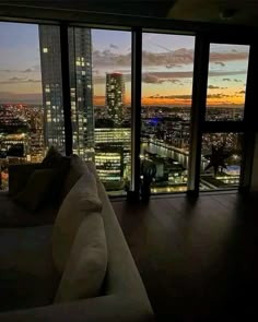 a living room filled with furniture and large windows overlooking the city at sunset or dawn