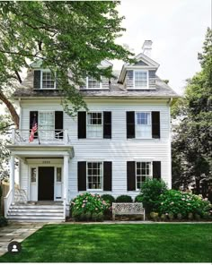 a large white house with black shutters on the front and side windows, surrounded by lush green grass