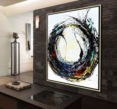 an abstract painting hangs on the wall next to a coffee table with a vase in front of it