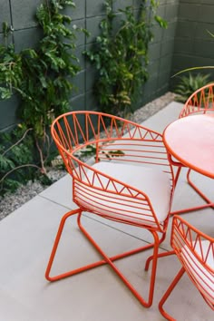 three orange chairs sitting next to each other on top of a cement floor near plants