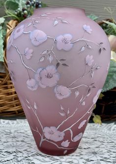 a pink vase sitting on top of a table next to a basket filled with flowers