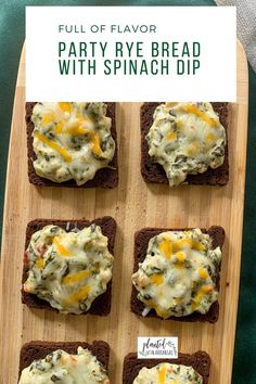 four pieces of bread with cheese and spinach spread on them, sitting on a cutting board