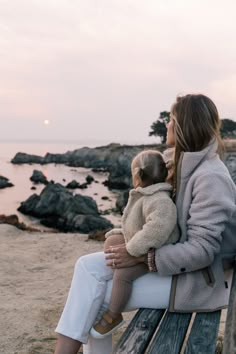 a woman sitting on top of a wooden bench next to a baby in her arms