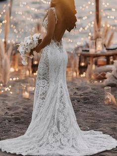 a woman in a wedding dress standing on the beach with her back to the camera