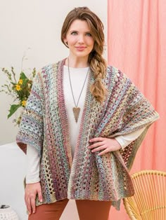 a woman standing in front of a pink curtain wearing a multicolored shawl