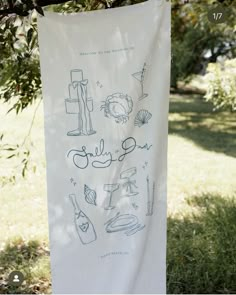 a white towel hanging from a tree in front of some grass and trees with drawings on it