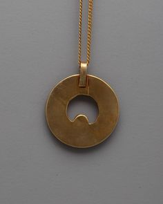 a gold necklace with a circular pendant hanging from it's side on a gray surface